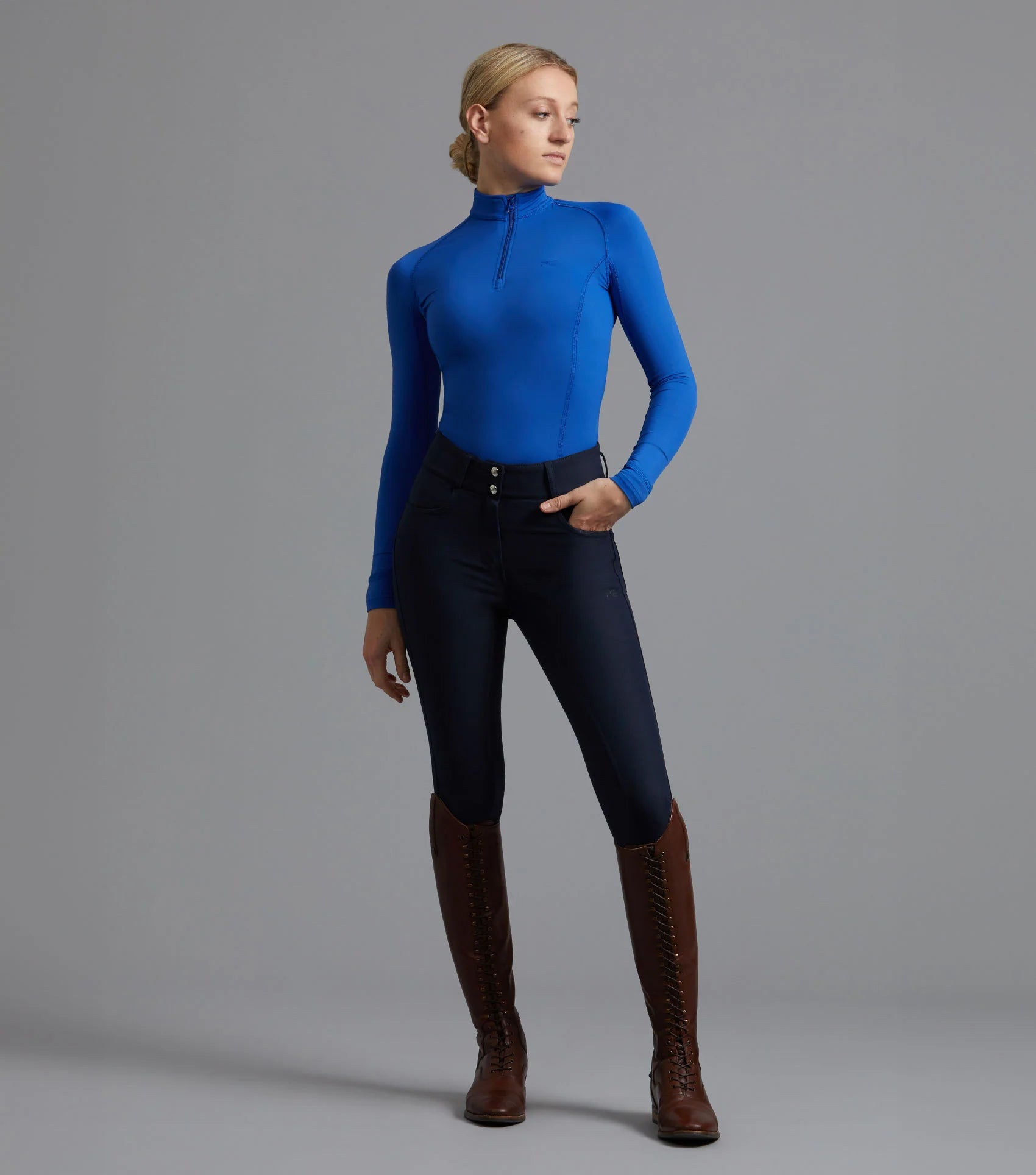 Premier Equine navy riding breeches. Woman in riding boots, full seat gel breeches, and blue riding top. Equiflair equestrian clothing.